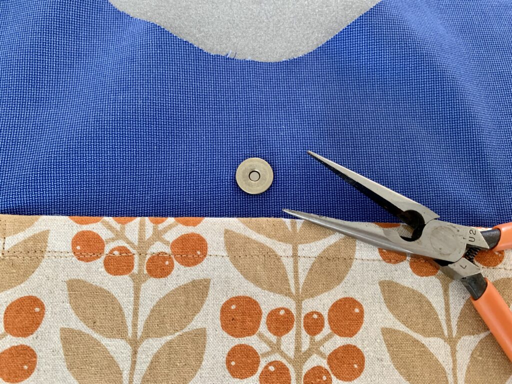 青い内布に柄物の布でポケットを縫い付け、ポケットの上にはマグネットボタンをつけたところ