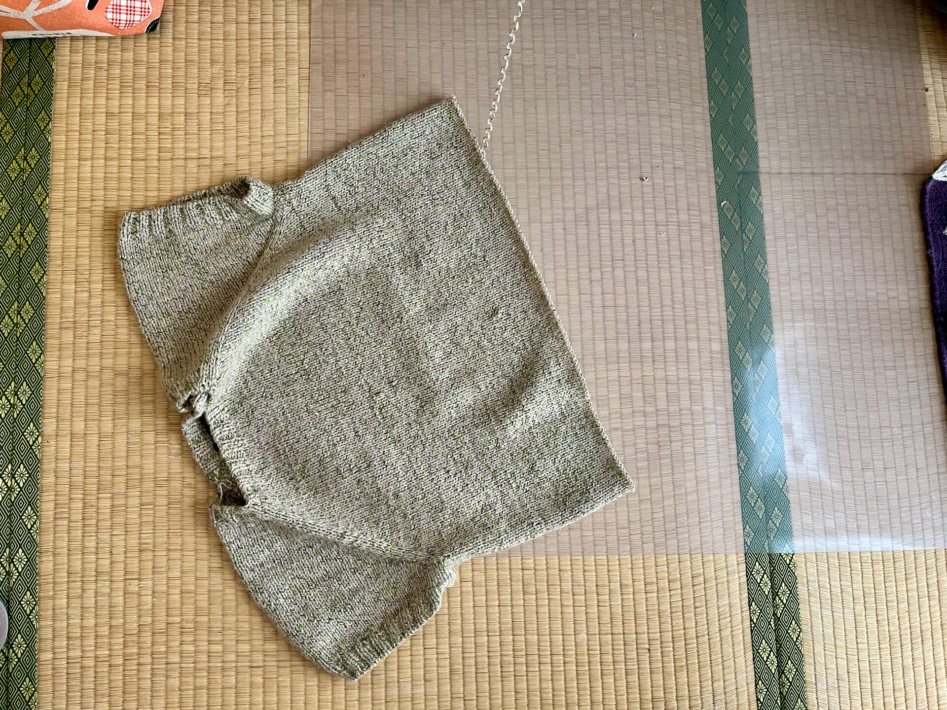 畳の上に広げた手編みのセーターを裾から解いている画像