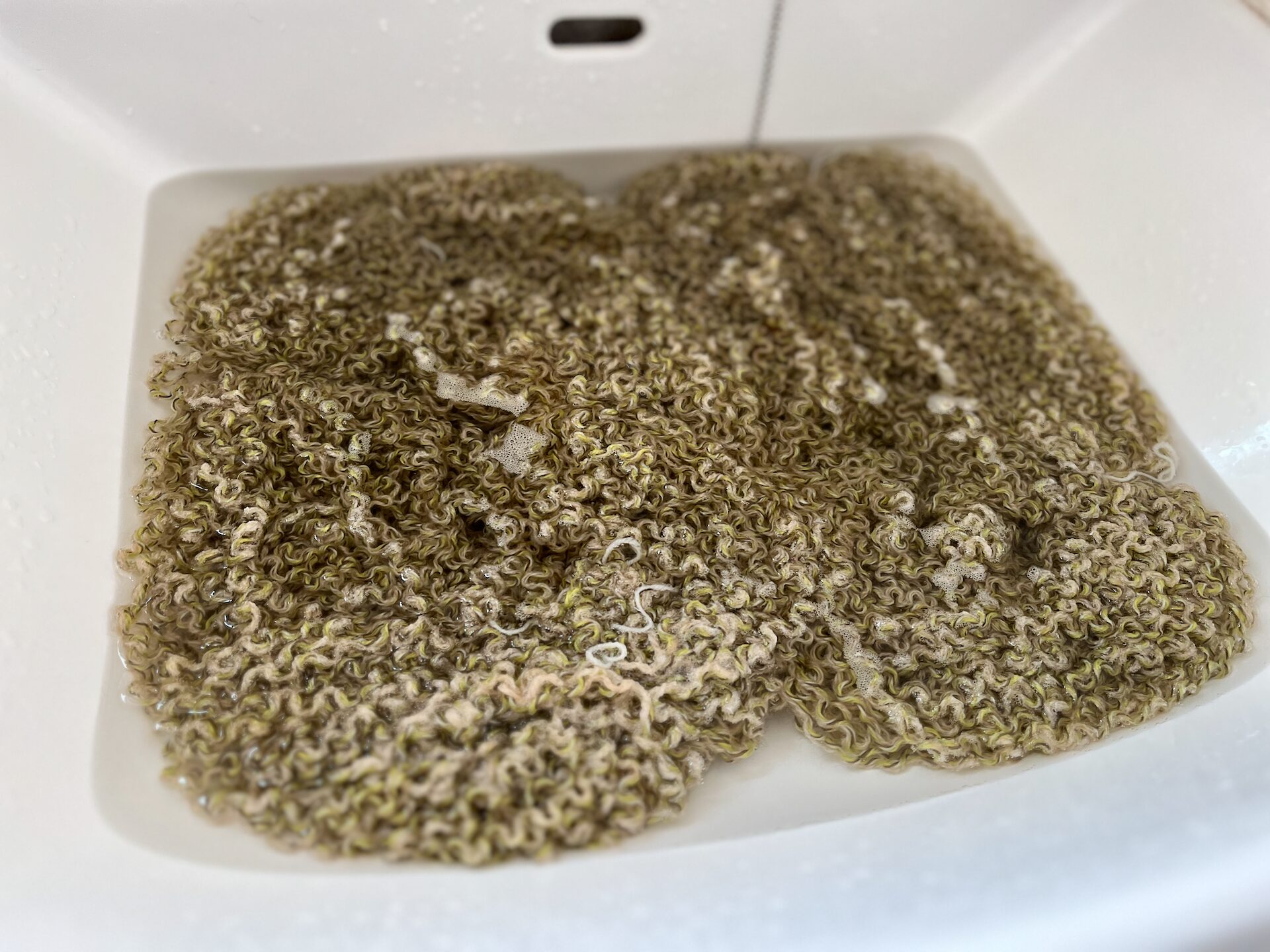 解いた緑色の毛糸を、白い陶器製のシンクで洗っている画像